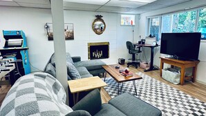 A living room with a sofa, a coffee table, a TV, and a foosball table. - Welcome to the Tree House apartment- a family friendly retreat with arcade games (Lake Forest Park)