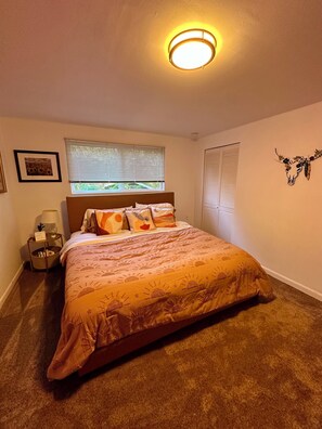 Ein Schlafzimmer mit einem Bett, einem Nachttisch, einer Lampe, einem Fenster mit Jalousien und einer Wanddekoration.