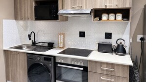 A modern kitchen with a dishwasher, oven, microwave, toaster, kettle, and a coffee station. - Luxury Rosebank Apartment  - Pool - Cinema - Backup Power - Secure Parking (Johannesburg)