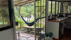 A room with a bed, a hammock, a dining area, and a view of the outdoors.