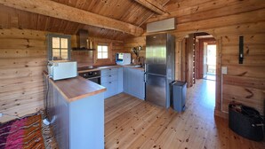 Interior de una cabaña de madera con cocina, que incluye un refrigerador, horno y pileta.