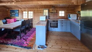 Interior de una cabaña de madera con comedor, cocina y un ventanal grande.