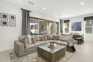 A modern living room with a sectional sofa, a coffee table, and a dining area with a table and chairs. - Monthly Stay| Resort Pool/Spa | Gym | Golf |Game Room | 3BR, Desert Willow (Palm Desert)