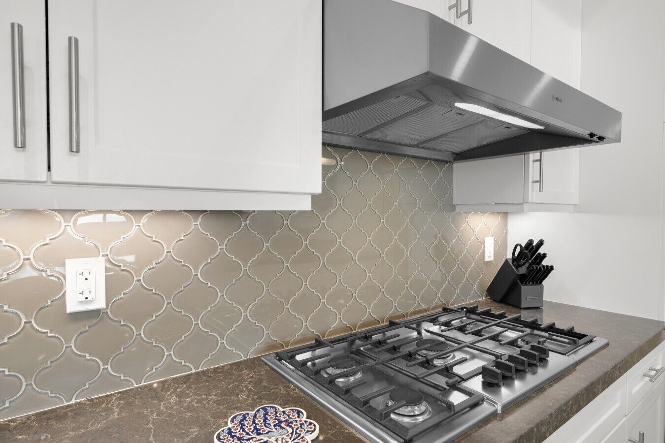 Una cocina con estufa a gas, armarios blancos, salpicadero con diseño y un juego de cuchillos.
