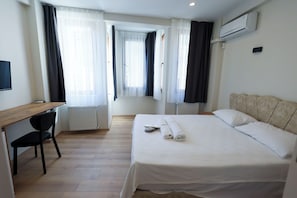 A hotel room with a bed, a desk, a chair, a radiator, and an air conditioning unit. - Taksim Heli Suites (Istanbul)