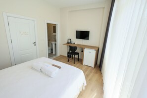A hotel room with a bed, a desk with a television, and a small refrigerator. - Taksim Heli Suites (Istanbul)
