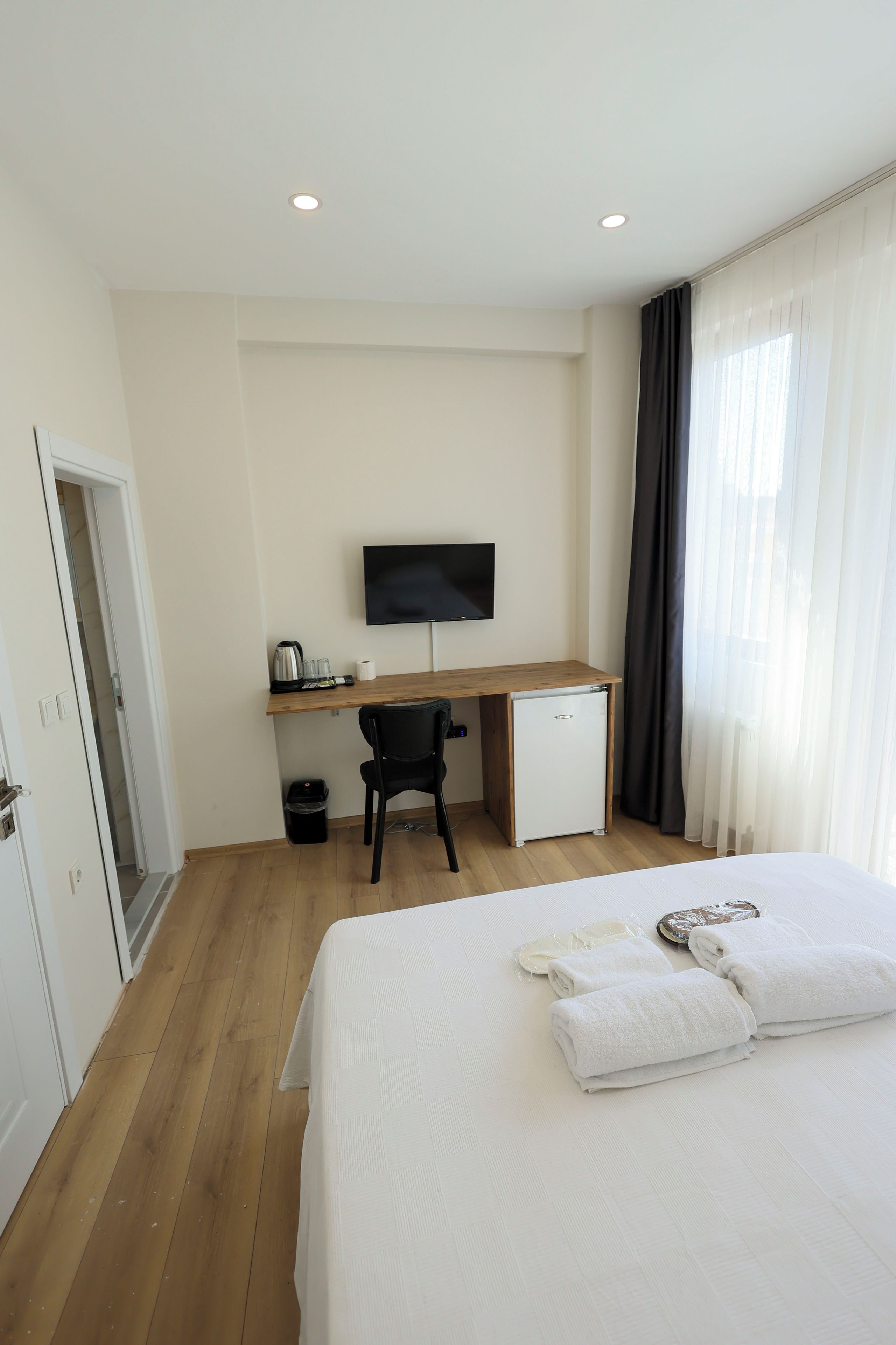 Ein Hotelzimmer mit Bett, Schreibtisch mit Computer, Stuhl, kleinem Kühlschrank und Fernseher an der Wand.