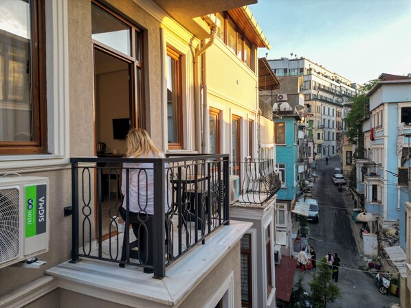 A balcony with a person standing, overlooking a street with buildings and parked cars. - Taksim Heli Suites (Istanbul)