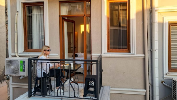 A balcony with a table and chairs, a window with a curtain, and an air conditioning unit. - Taksim Heli Suites (Istanbul)