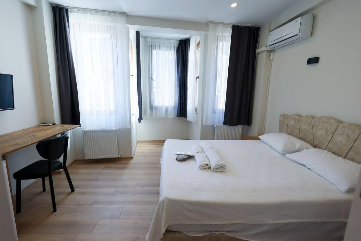 A hotel room with a bed, a desk, a chair, and a window with curtains.