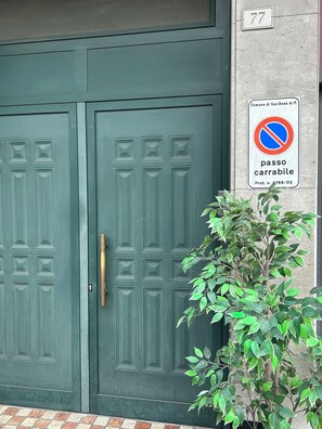Puertas verdes dobles con un letrero de ‘prohibido estacionar’, una planta pequeña y el número 77.