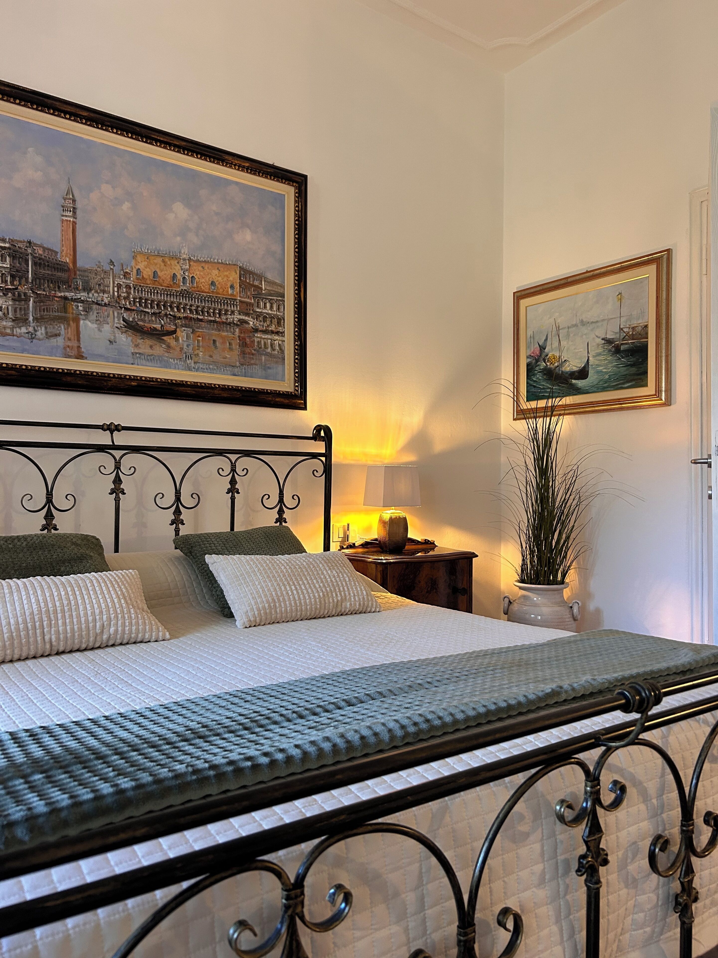 Un letto rifatto con cura, un comodino con una lampada e due quadri appesi al muro.