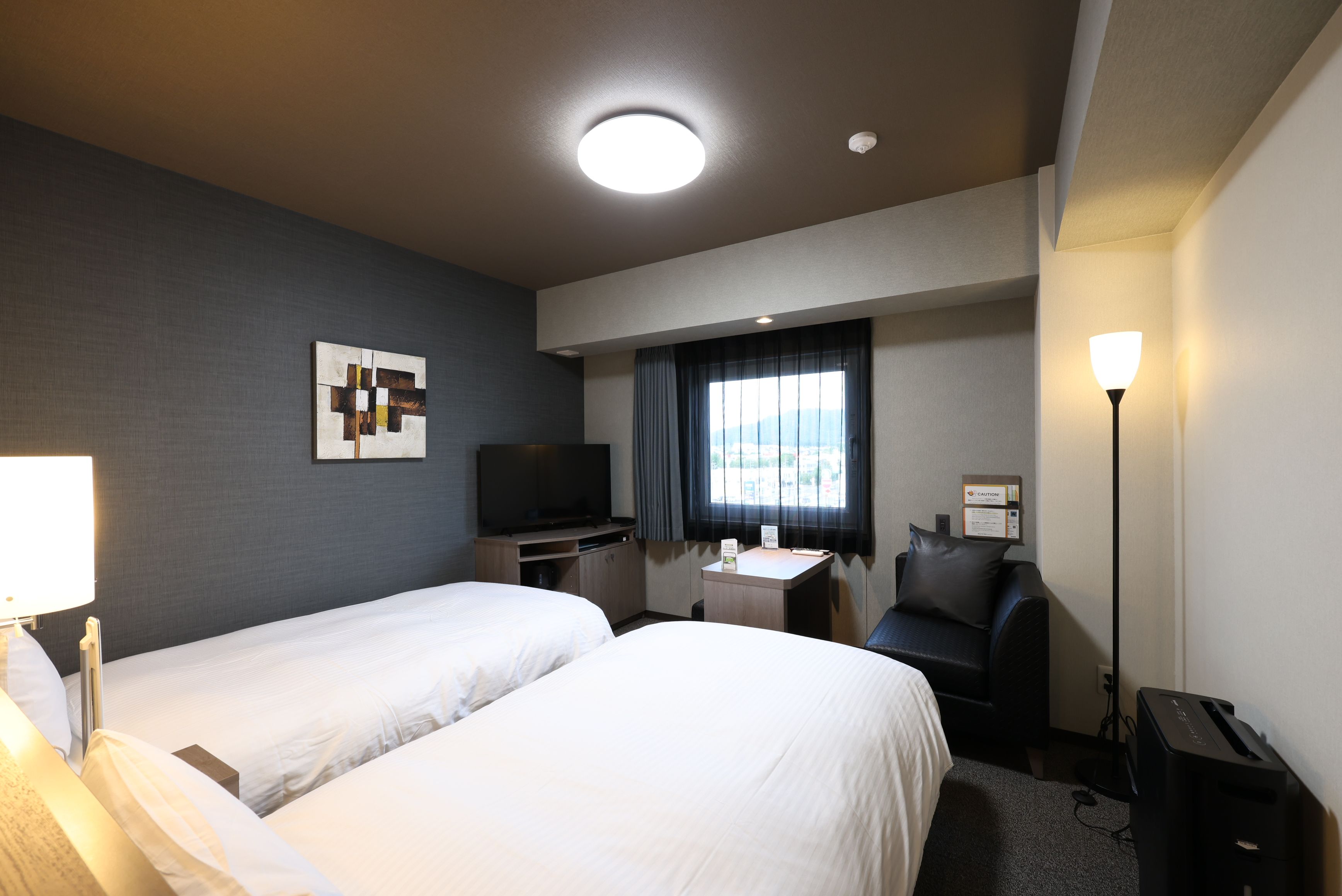 A hotel room with two beds, a desk, a television, a chair, a lamp, and a window with curtains.