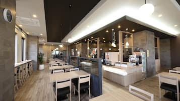 A modern restaurant interior with wooden tables and chairs, a counter with a coffee machine, and pendant lighting.