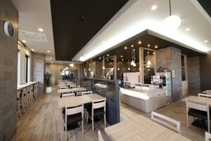 Un interior de restaurante moderno con mesas y sillas de madera, una barra con máquina de café e iluminación colgante.