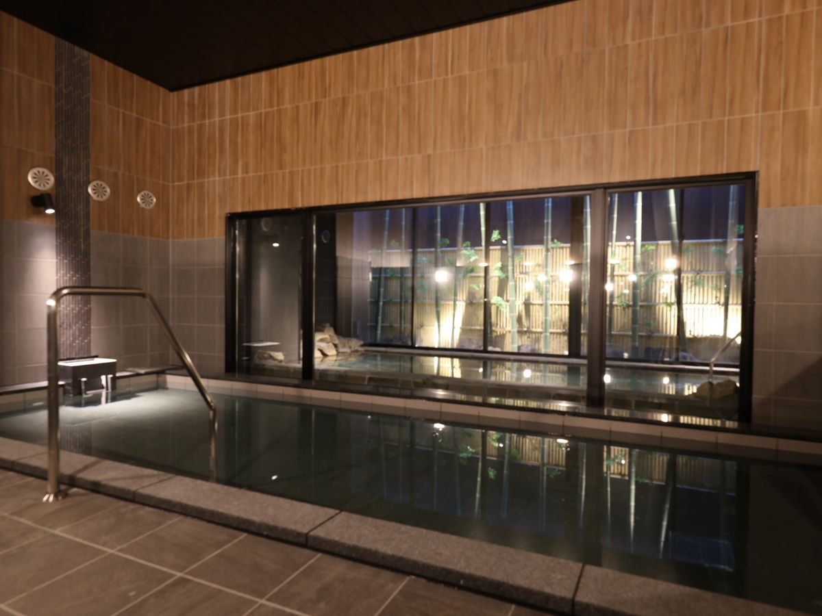 A swimming pool with a glass wall, a metal ladder, and a view of the outside.