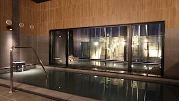 Una piscina con pared de vidrio, escalera metálica y vistas al exterior.