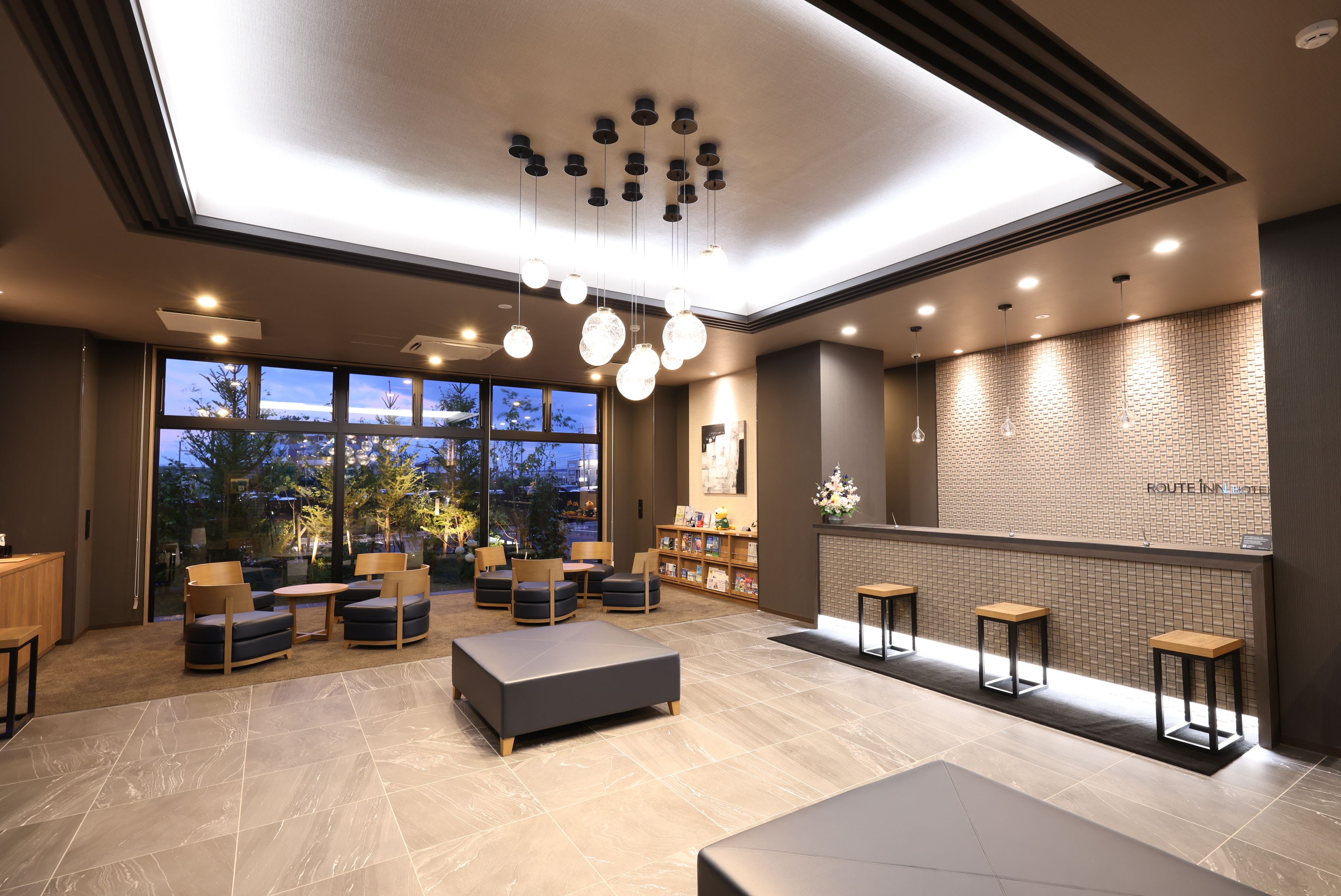 A modern hotel lobby with a seating area, a reception desk, and a view of the outdoors.