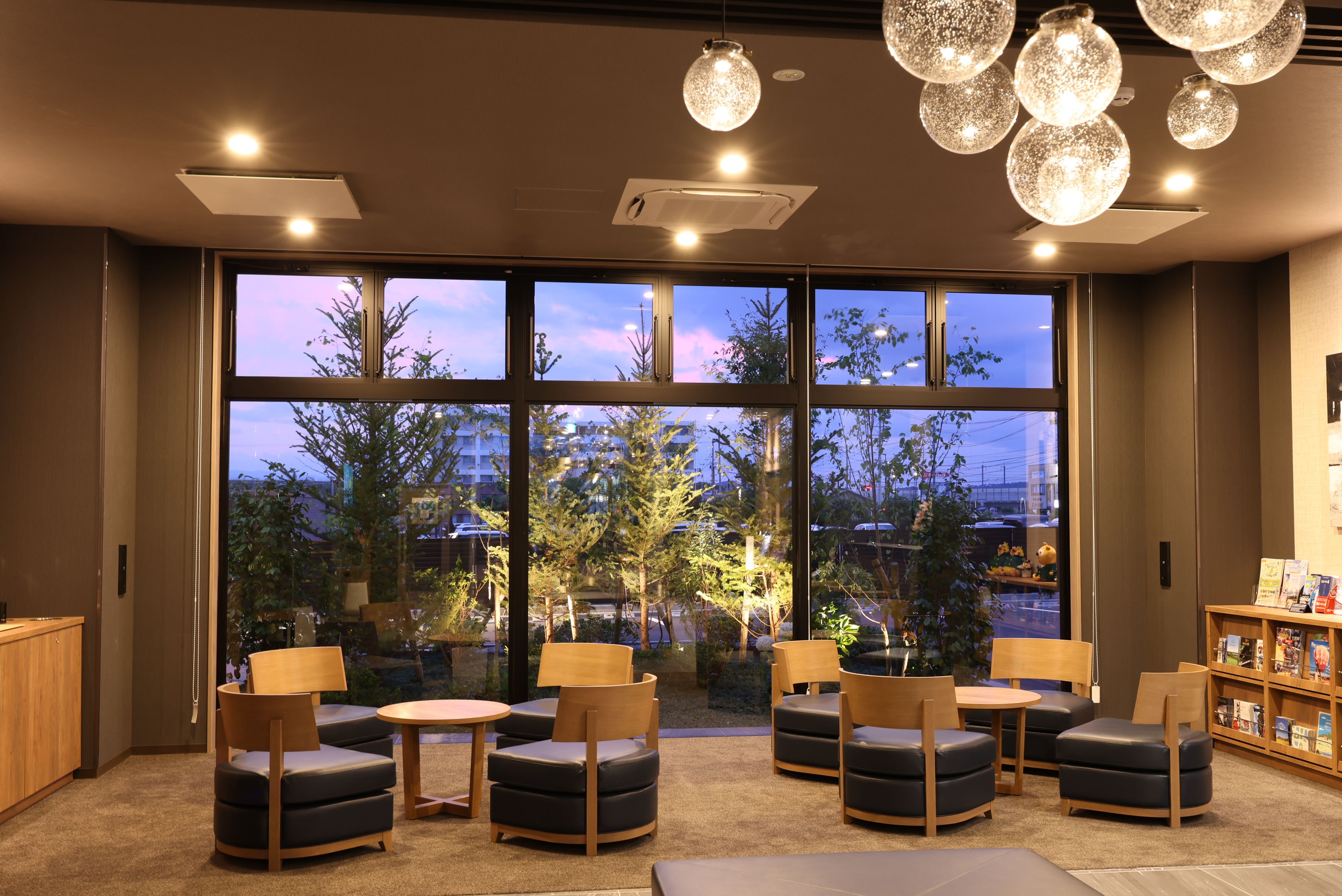 A modern lounge area with multiple seating options, large windows offering a view of the cityscape, and ambient lighting fixtures.