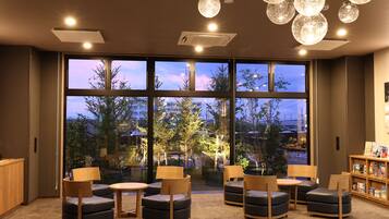 A modern lounge area with multiple seating options, large windows offering a view of the cityscape, and ambient lighting fixtures.
