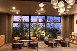 Uma área de estar moderna com diversas opções de assento, janelas amplas com vista para a paisagem urbana e luminárias com iluminação suave.