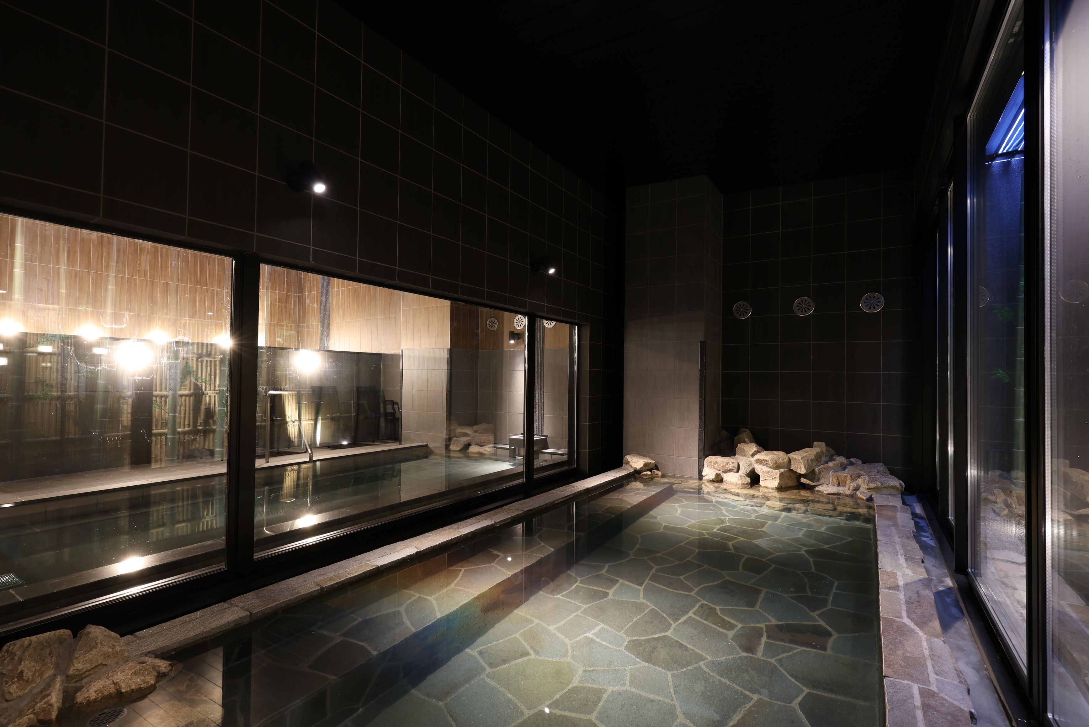A modern interior with a stone-tiled floor, a glass partition, and a seating area with a bench and a table.