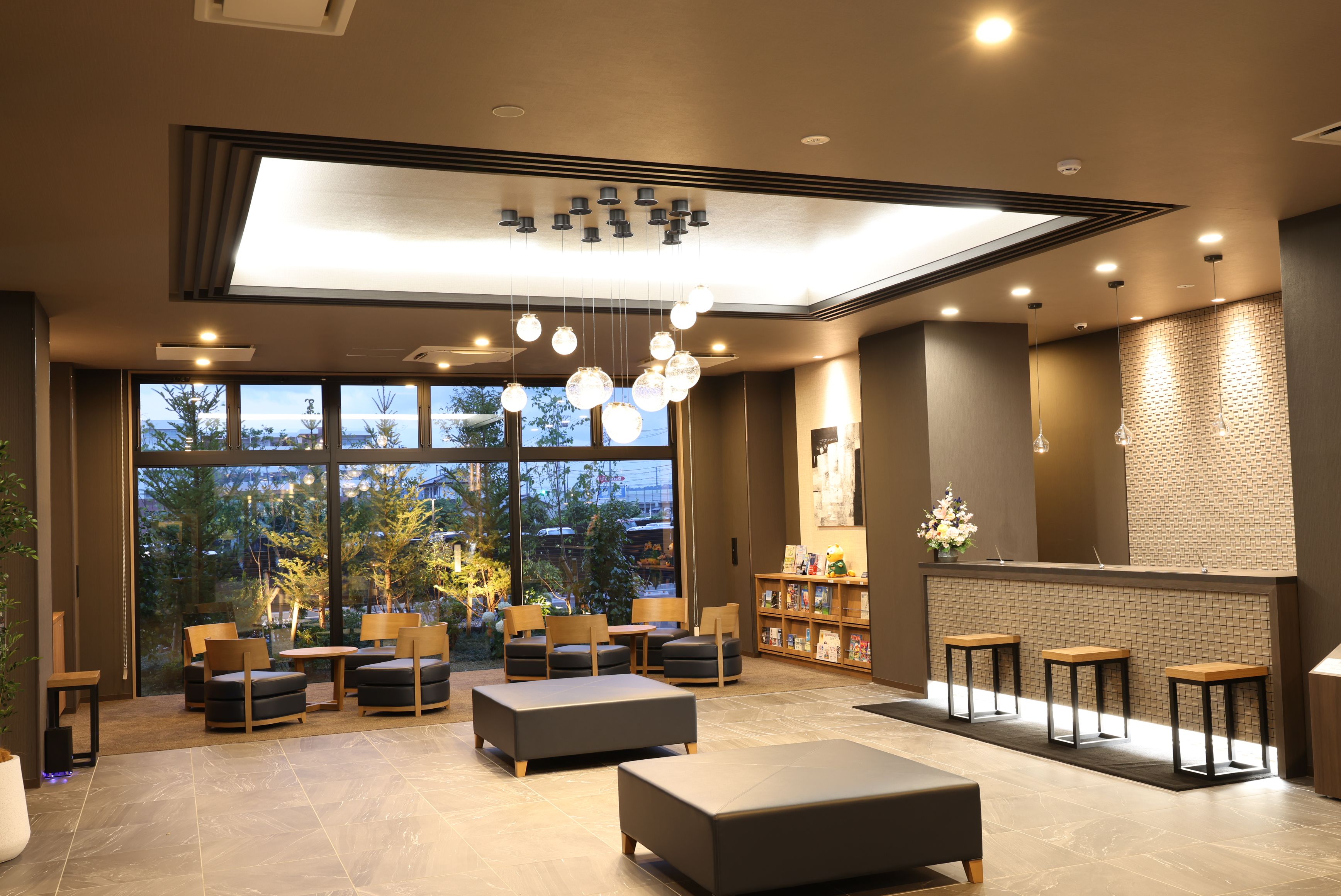 A modern interior with seating, a reception desk, and large windows offering a view of the outdoors.