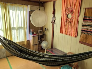 A room with a hammock, a fan, a desk with a computer, and a wall with decorative items.