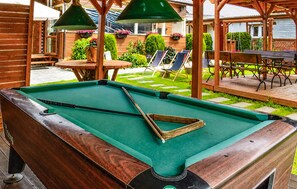 Ein Billardtisch mit Spielzeug und einer Dreieckshalterung, umgeben von Holzmöbeln und Gartenmöbeln.