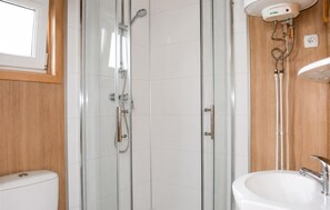 Ein Badezimmer mit einer gläsernen Duschkabine, einem weißen Waschbecken und einer Wandpaneelaus Holz.