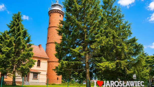 Une tour en briques surmontée d’une horloge, un bâtiment avec un toit rouge et une enseigne sur laquelle on peut lire : « J’♥ JAROSLAWIEC ».