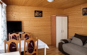 Ein Zimmer mit Holzwandverkleidung, einem Fernseher, einem Esstisch mit Stühlen, einer Couch und einem Kleiderschrank.