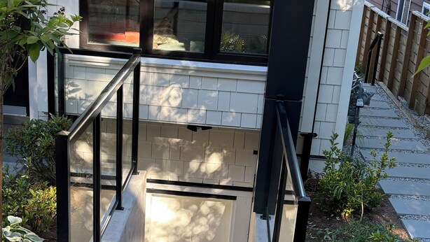 Entrada residencial com escadaria de concreto, grades de metal, um pequeno jardim e um tapete com a palavra 'hello'.