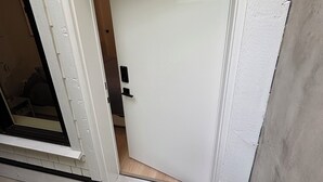 Uma porta branca com um tapete de entrada preto com a palavra 'hello' e uma pequena janela à esquerda.