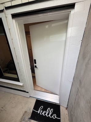 A white door with a black doormat reading 'hello' and a small window to the left.