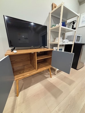 Un espace de vie compact comprenant un meuble de rangement en bois servant d’unité multimédia, un téléviseur à écran plat et des étagères intégrées.