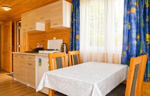 Kompakti keittiö, jossa on puiset kaapit, liesi ja pesuallas. Keittiössä on ruokapöytä tuoleineen sekä ikkuna, jossa on verhot.