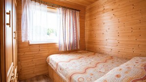 Une petite pièce en bois avec un lit simple, une fenêtre avec des rideaux et une porte.