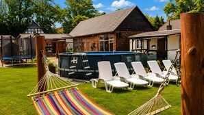 Un espace verdoyant avec un hamac, des chaises longues blanches et une piscine.