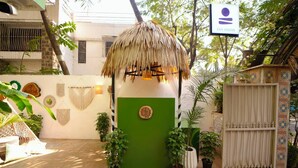A thatched-roof structure with a green door, potted plants, and a sign reading 'ZEN COLIVE'. - Zen Colive (Pune)