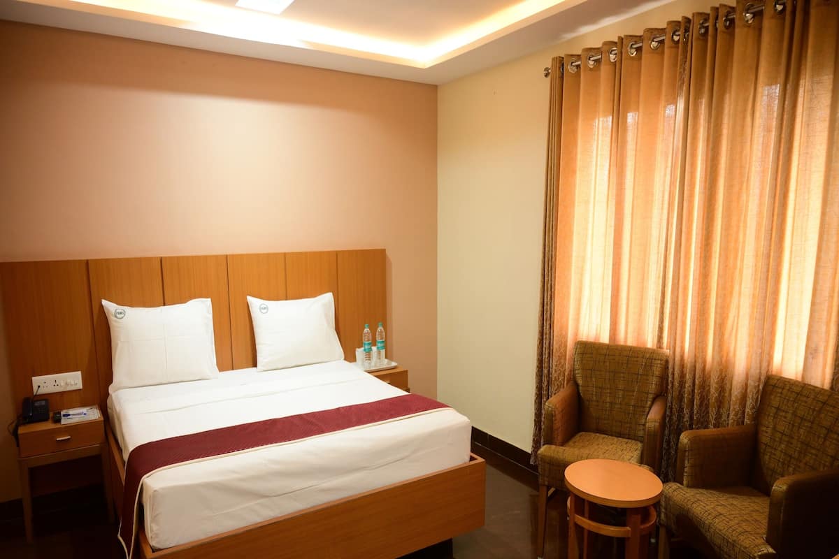 A hotel room with a wooden bed, a nightstand with a phone, a chair, a small table, and a window with curtains.