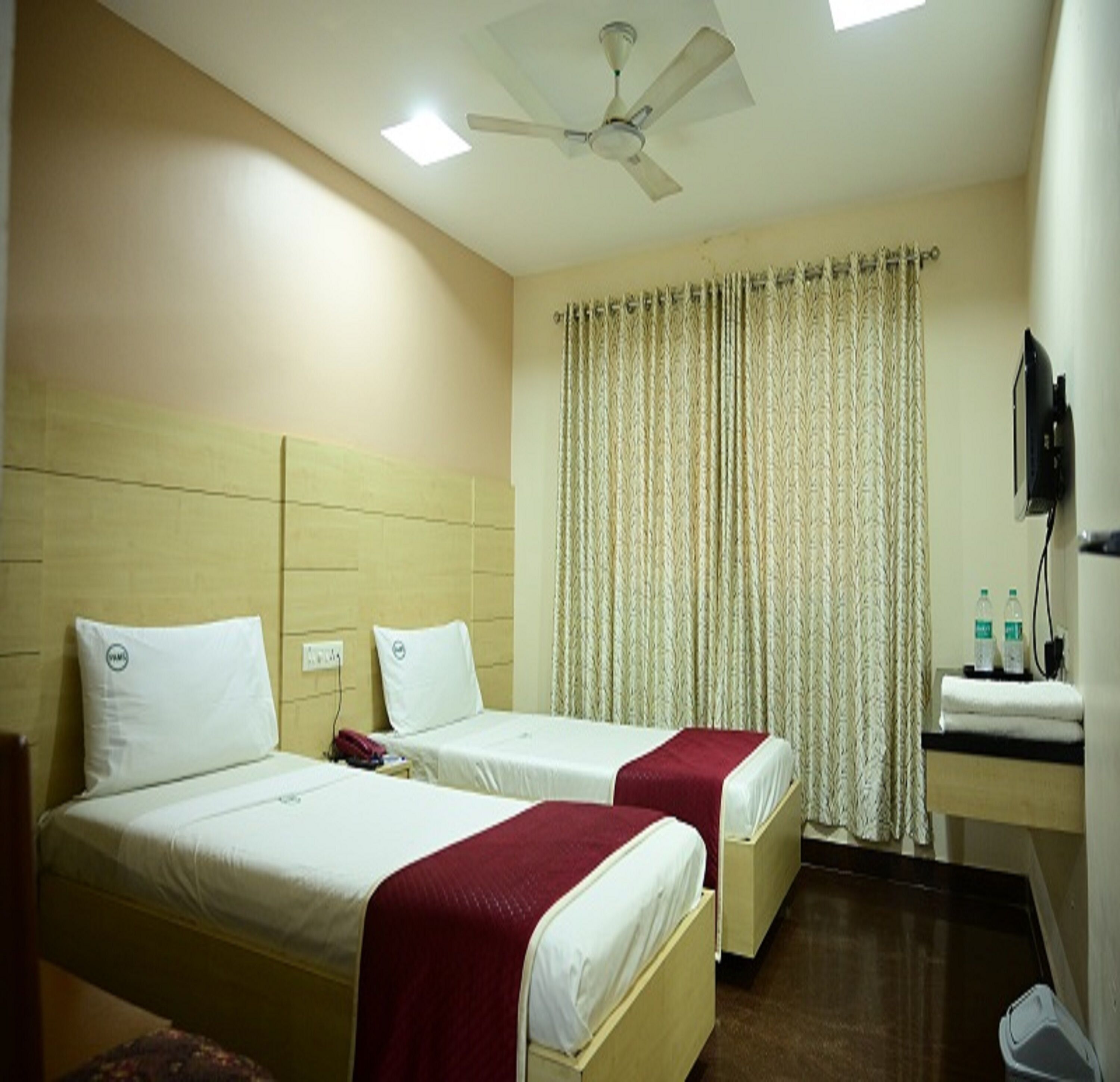 Habitación de hotel con dos camas, ventilador de techo, televisor y ventana con cortinas.