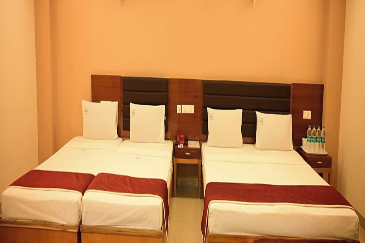 A hotel room with two beds, a wooden headboard, bedside tables with water bottles, and a ceiling light fixture.