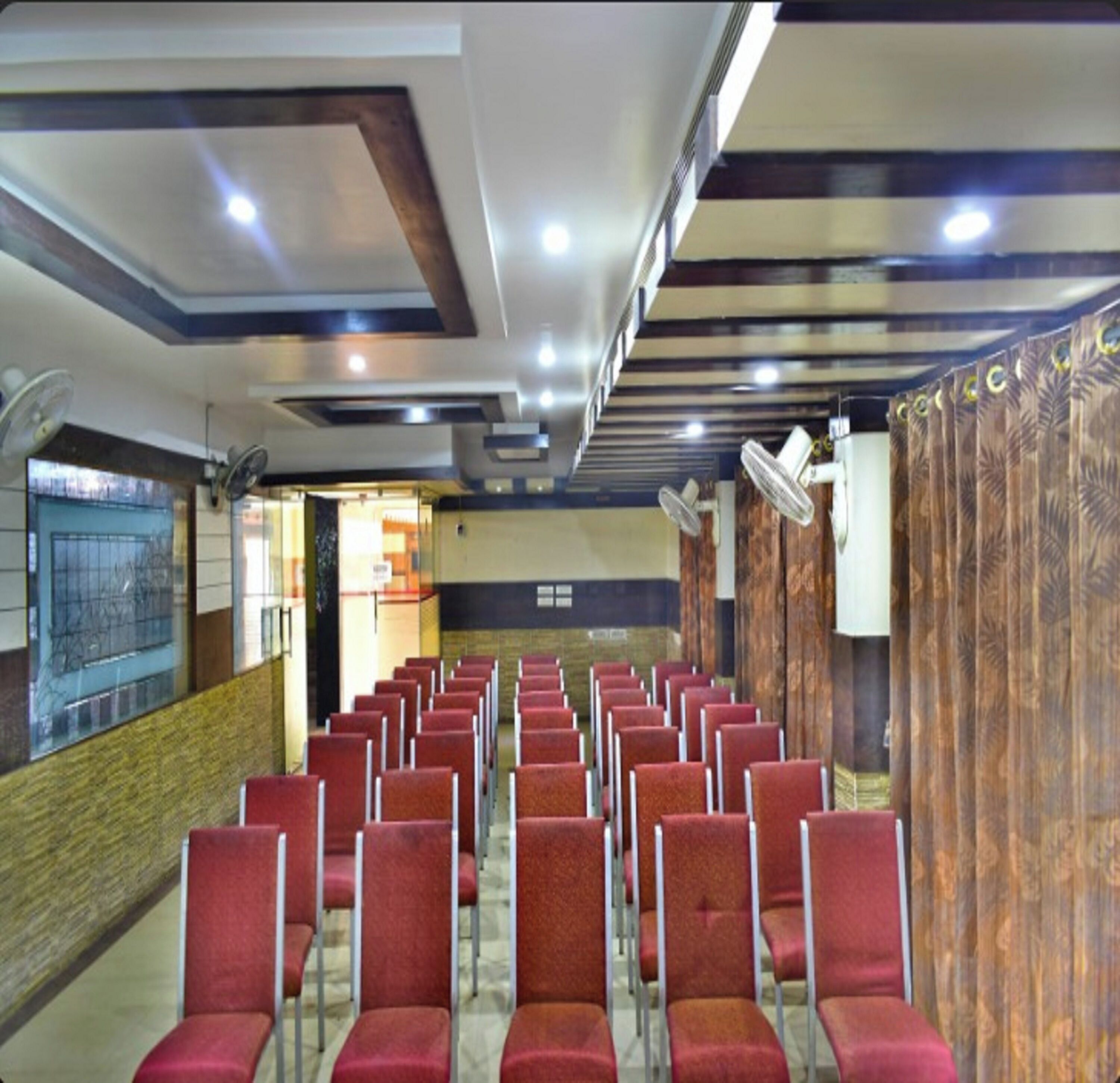 A conference room with rows of red chairs, ceiling fans, and a patterned curtain.