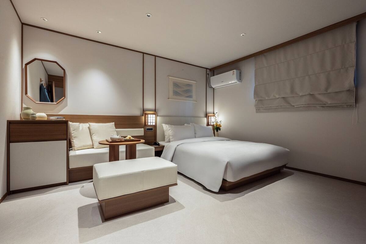 Hotelkamer met een bed, nachtkastje, stoel, bureau, spiegel en een airconditioning.