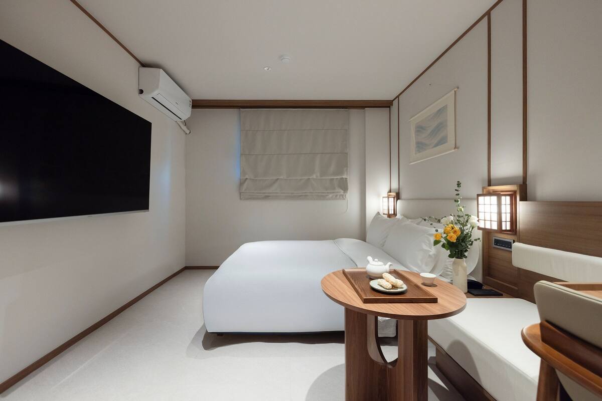 Een moderne hotelkamer met een bed, nachtkastje, lamp en kunstwerk.