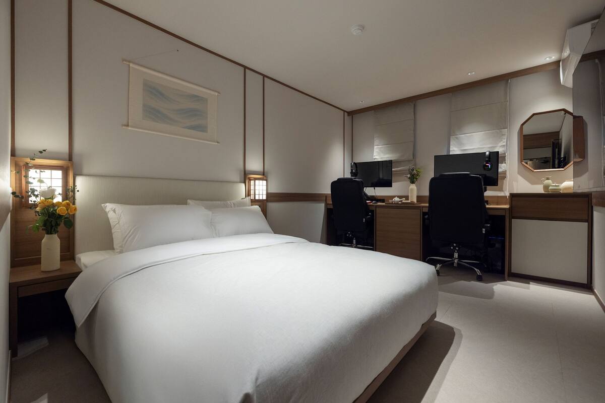 Een hotelkamer met een groot bed, een bureau met een computer, een stoel, een televisie en een spiegel.