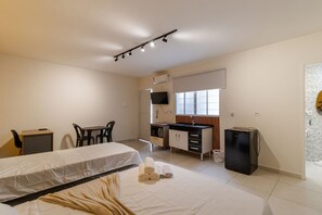 Habitació d'hotel amb un llit, escriptori, cadira, petita cuina i televisió.