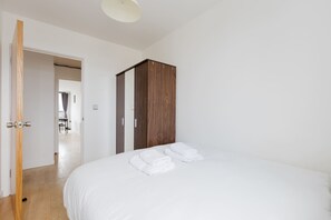 A bedroom with a bed, a wooden wardrobe, and a door leading to another room. - 2BDR Flat with Skyline Views in East London (Greater London)