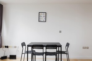 Ein Essbereich mit Tisch, vier Stühlen, einer Steckdose und einem gerahmten Bild an der Wand.
